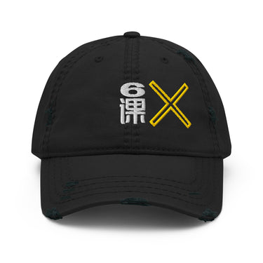 A black distressed baseball cap shown from the front. The cap features an embroidered graphic on the front that includes a white stylized character or symbol to the left, and a bright yellow "X" to its right. The cap has intentional rips and fraying on the brim and crown, giving it a worn look.