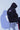 A person sits on a stool with their back to the camera, wearing a solid-colored hoodie with the hood up. The back of the hoodie features several scattered, high-contrast graphics with an abstract, "glitch" aesthetic.