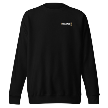 Front view of an sweatshirt in black. A minimalist design placed on the upper left chest shows a compact arrangement of small graphic elements, including a circular icon, the word “KRAMPUS” in bold, and a narrow vertical block with stylized symbols.
