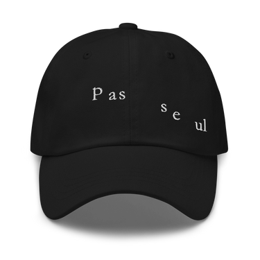 Front view of a baseball cap in black. The words "pas seul" are embroidered across the front panel in white, the letters set in a fine serif and scattered so they step down and to the right. The cap is an unstructured low-profile six-panel in smooth chino twill, with embroidered eyelets and an adjustable metal buckle strap.