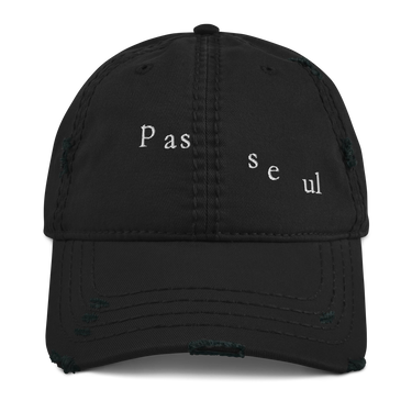 Front view of a distressed hat in black. The words "pas seul" are embroidered across the front panel in white, the letters set in a fine serif and scattered so they step down and to the right. The cap is an unstructured low-profile six-panel with a curved, stitched brim and a soft pre-shrunk twill crown.
