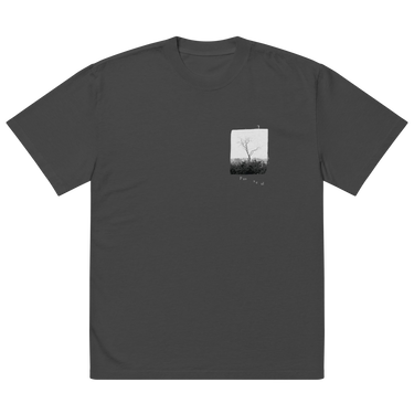 Front view of an oversized tee in faded black. A small halftoned panel sits on the left chest: a bare, leafless tree standing over dark undergrowth, printed with a woven fabric texture and rough torn edges. Below it the words "pas seul" are set in a fine serif, the letters scattered and stepping down to the right.
