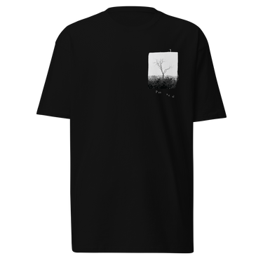 Front view of a t-shirt in black. A small halftoned panel sits on the left chest: a bare, leafless tree standing over dark undergrowth, printed with a woven fabric texture and rough torn edges. Below it the words "pas seul" are set in a fine serif, the letters scattered and stepping down to the right.
