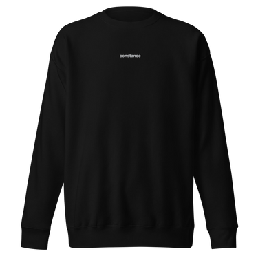 Front view of an sweatshirt in black. Minimal design featuring a small white lowercase word “constance” centered across the upper chest. The typography is clean and modern, standing out subtly against the solid black fabric.