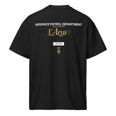 Back view of a box tee in Black. A stacked graphic fills the upper back: "AIRSPACE PATROL DEPARTMENT" in heavy white capitals, "GLORIA NOS DUCIT" in smaller gold capitals beneath it, then "L'Azur" in a large gold script with a long trailing flourish. Below sit a small white box lettered "FIRST SPEAR" in black, a weathered gold seal stamp carrying two characters, and "gen 5" in gold.