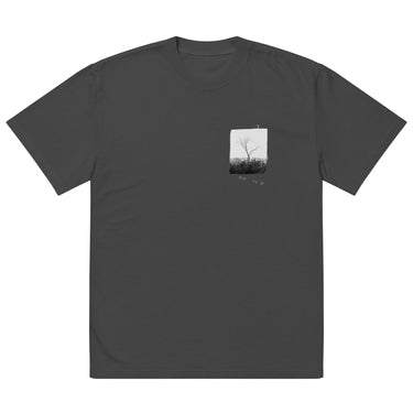 Front view of an oversized tee in faded black. A small halftoned panel sits on the left chest: a bare, leafless tree standing over dark undergrowth, printed with a woven fabric texture and rough torn edges. Below it the words "pas seul" are set in a fine serif, the letters scattered and stepping down to the right.