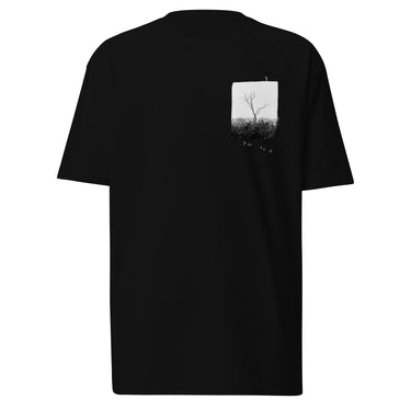 Front view of a t-shirt in black. A small halftoned panel sits on the left chest: a bare, leafless tree standing over dark undergrowth, printed with a woven fabric texture and rough torn edges. Below it the words "pas seul" are set in a fine serif, the letters scattered and stepping down to the right.