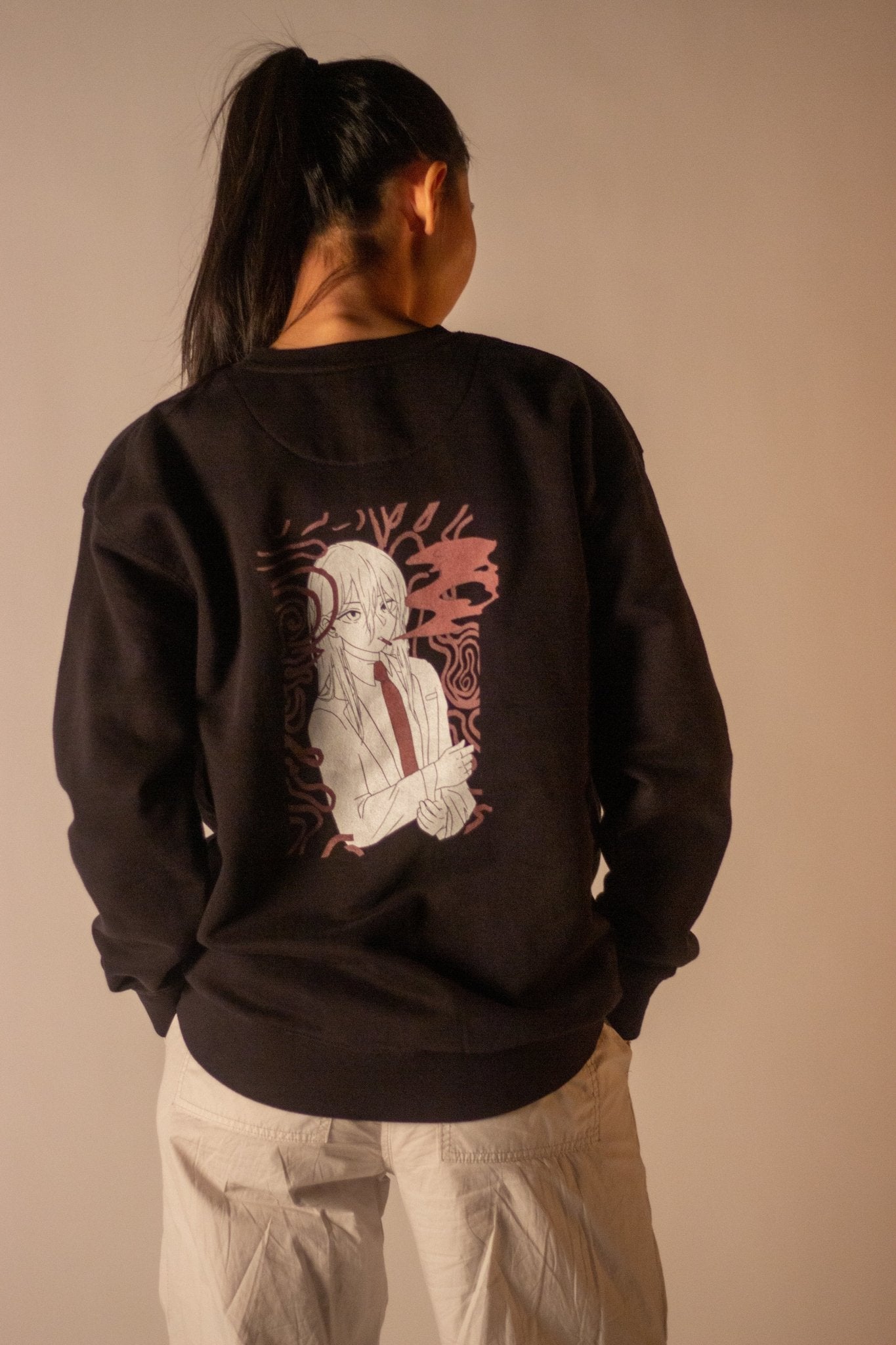 Back view of a model wearing a black sweatshirt. The shirt features a large graphic of a female anime character with a red tie, set against a pink and black abstract background.