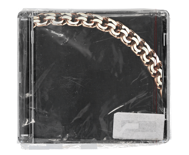 CD jewel case in clear shrink wrap. The cover is black with a heavy rose-gold chain curving across the top corner, with a silver security tag in the lower corner.