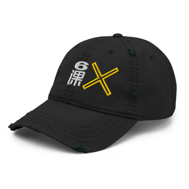 A black distressed baseball cap shown from a front-left angle. The cap features an embroidered graphic on the front with a white stylized character or symbol and a yellow "X", partially visible. The cap has intentional rips and fraying on the brim and crown.