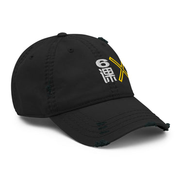 A black distressed baseball cap shown from a front-right angle. The cap features an embroidered graphic on the front with a white stylized character or symbol and a yellow "X", partially visible. The cap has intentional rips and fraying on the brim and crown.