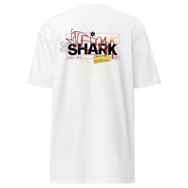 Back view of a solid-colored shirt. A large, chaotic collage graphic on the upper back features the word "SHARK" in a bold font. The design is layered with various handwritten signatures, sketchy scribbles, and abstract background patterns.