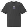 The front of a faded black oversized t-shirt. Centered on the chest is a small graphic featuring a stylized white symbol, resembling a chalice, set against a blue rectangular background.