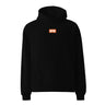 Black oversized hoodie, front view, featuring a small centered orange rectangular logo with a stylized white 'M' inside.