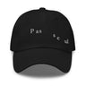 Front view of a baseball cap in black. The words "pas seul" are embroidered across the front panel in white, the letters set in a fine serif and scattered so they step down and to the right. The cap is an unstructured low-profile six-panel in smooth chino twill, with embroidered eyelets and an adjustable metal buckle strap.