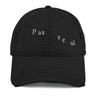 Front view of a distressed hat in black. The words "pas seul" are embroidered across the front panel in white, the letters set in a fine serif and scattered so they step down and to the right. The cap is an unstructured low-profile six-panel with a curved, stitched brim and a soft pre-shrunk twill crown.