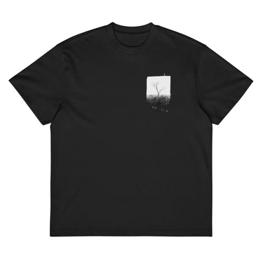 Front view of a box tee in black. A small halftoned panel sits on the left chest: a bare, leafless tree standing over dark undergrowth, printed with a woven fabric texture and rough torn edges. Below it the words "pas seul" are set in a fine serif, the letters scattered and stepping down to the right.