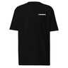 Front view of an t-shirt in black. A minimalist design is placed on the upper left chest, featuring a compact arrangement of graphic elements. The word “KRAMPUS” appears in small white uppercase lettering, paired with a circular gold icon to its left. 