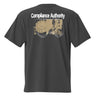 Back view of an oversized tee in black. A large graphic composition spans the upper back, featuring the phrase “Compliance Authority” in bold at the top, with a date range centered beneath it. Below, a rectangular collage combines a textured illustration of a dial-like object and a stylized figure, framed by vertical bars with additional characters. Thin linework of symmetrical wings extends outward from the bottom edge of the collage, adding contrast to the overall layered design.