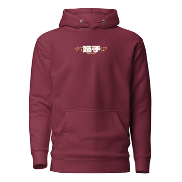 Front view of a Hoodie in Maroon. a small chest graphic pairing a gold cursive wordmark partially overlaid by a bold white stylized emblem, with a block-letter word underneath in the same gold tone