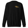 Front view of an sweatshirt in black. Design is positioned on the upper left chest. Design features a yellow rectangular label reading “CONNECKEN,” smaller text “DER WÄCHTER,” and fine white script lines and coordinates below it.