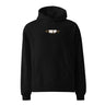 Front view of a Oversized Hoodie in Black. a small chest graphic pairing a gold cursive wordmark partially overlaid by a bold white stylized emblem, with a block-letter word underneath in the same gold tone
