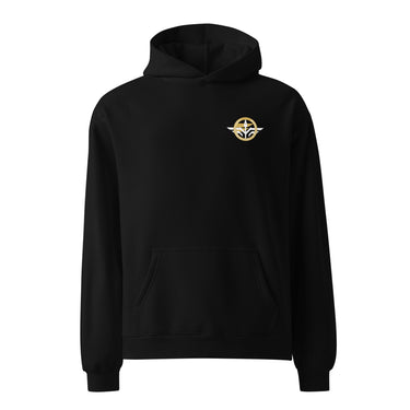 Front view of an oversized hoodie in Black. A small circular emblem sits on the left chest: a gold ring lettered "MIRACULUM IN CAELO NUMQUAM CADET" in white capitals, with a white winged spearhead standing through its centre and swept wings running out to either side.