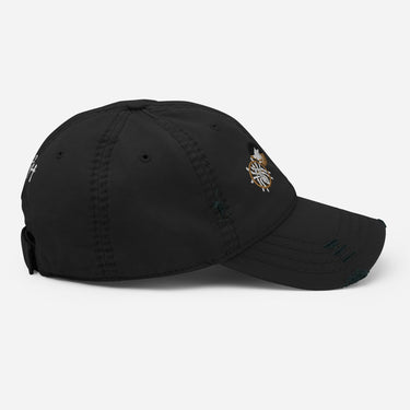 A side profile view of a solid-colored, distressed hat, showing the various embroidered emblems on the front and side, and the script monogram on the back.